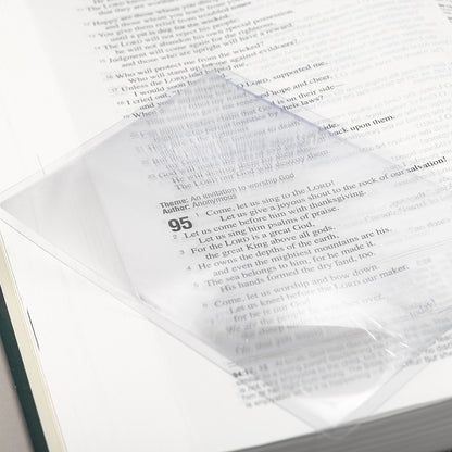 Clear pocket square magnifying sheet with 150% magnification, placed on book page showing text details