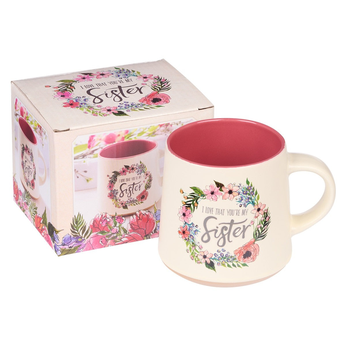 Ceramic coffee mug with pink interior and floral wreath design reading “I love that you’re my sister” with gift box