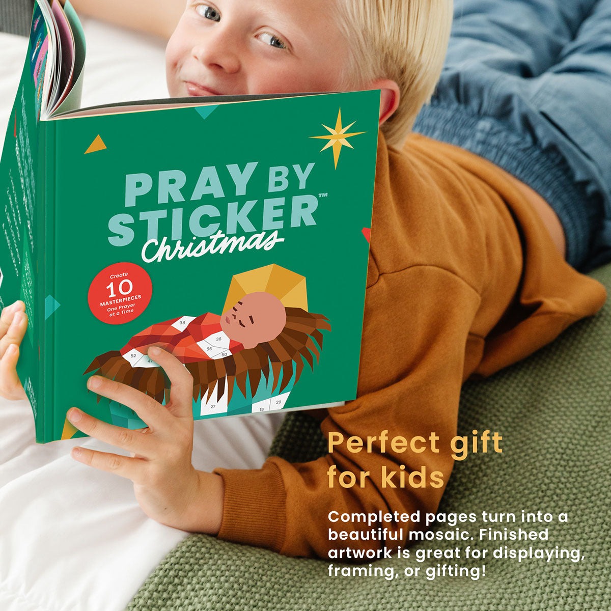 Child holding green "Pray by Sticker Christmas" activity book with nativity illustration on cover and holiday stars design