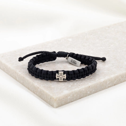 Black woven Strength Bracelet for men with silver cross charm and faith tag on white marble background