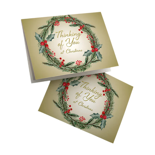 Christmas card with holly and pine wreath design, gold "Thinking of You at Christmas" text on beige background