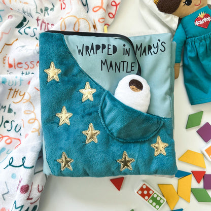 Soft blue fabric "Wrapped in Mary's Mantle" quiet book with gold stars and small baby figure in pocket