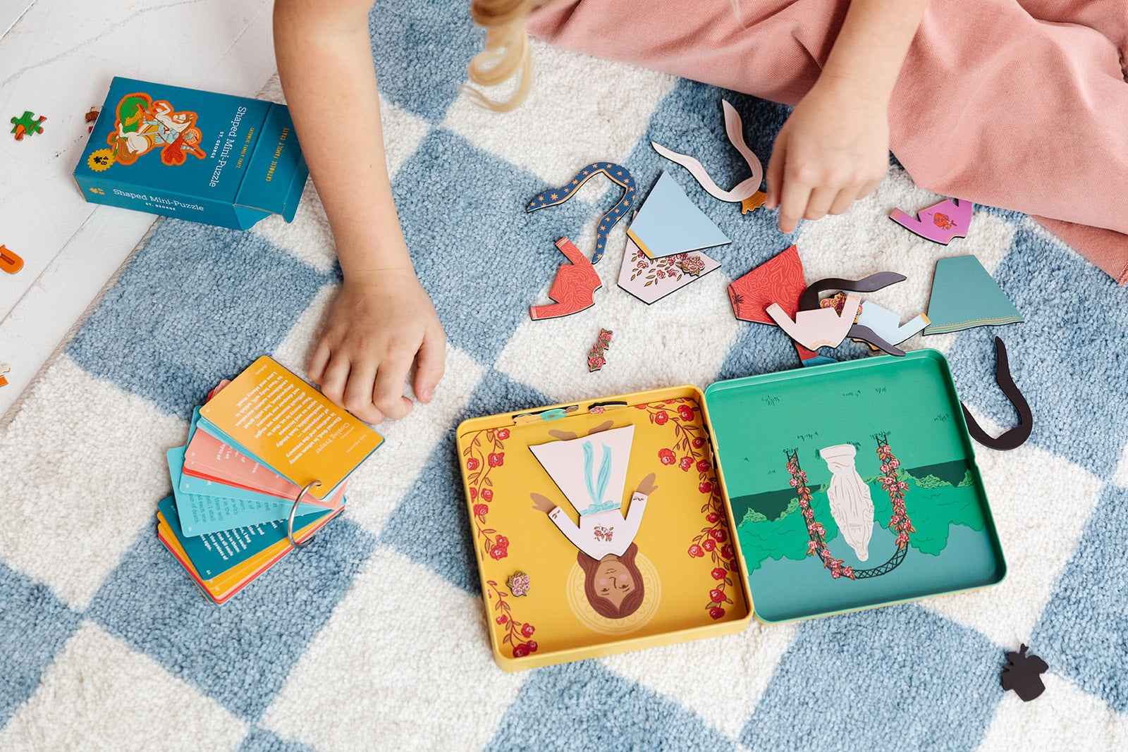 Child playing with illustrated Mary Dress Up Magnet Playset pieces and foldable magnet book on blue checkered rug