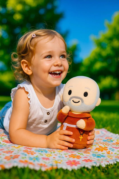 Young child smiling and holding Saint Padre Pio plush doll with brown robe and rosary outdoors on floral blanket